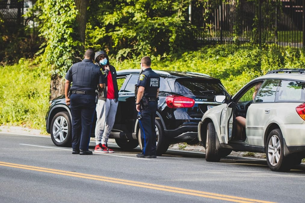 man in black t-shirt and black pants standing beside black suv during daytime after a car accident