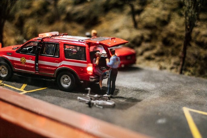 a miniature scene of a red car accident with a man standing next to it who needs a car accident lawyer