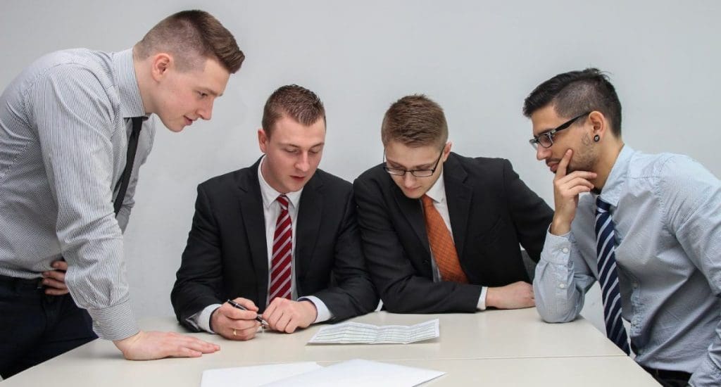 four men looking to the paper on table